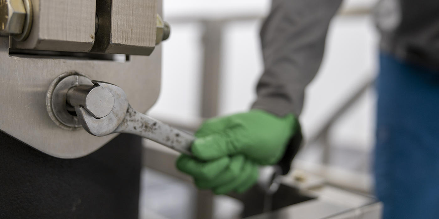 Worker wearing green gloves applying a wrench to a bolt on a piece of equipment