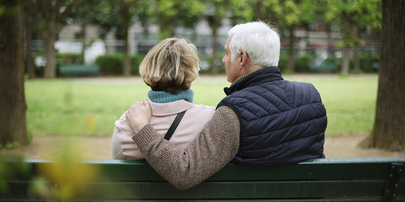 Photo of older couple sitting on park bench, their backs to the camera