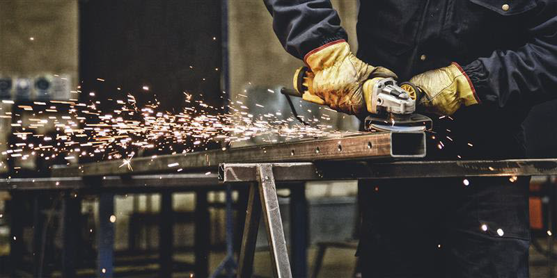 Worker using handheld grinder on metal, causing sparks