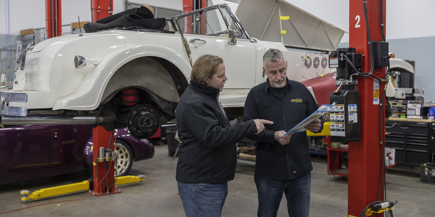 Worker and customer discussing vehicle raised by autolift behind them