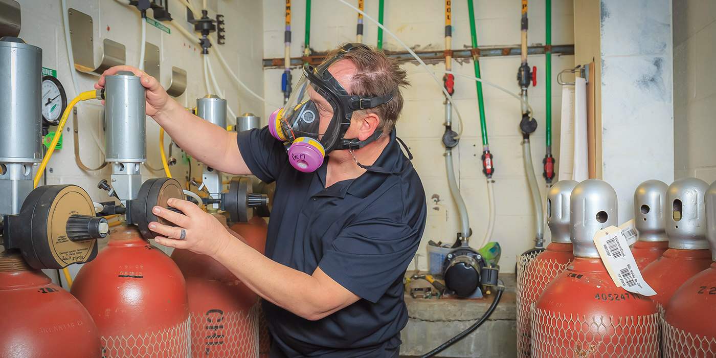 Worker in full-face respirator checking cylinders of gases in a workroom